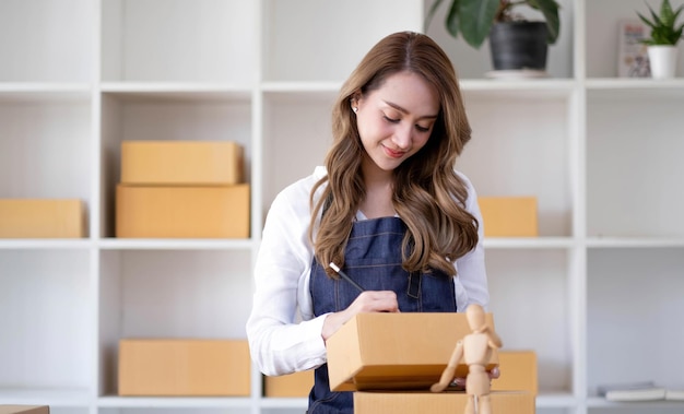 Empresária asiática bem-sucedida com caixas de encomendas em seu próprio emprego, comprando negócios on-line no escritório em casa, iniciando o conceito de pequenas empresas