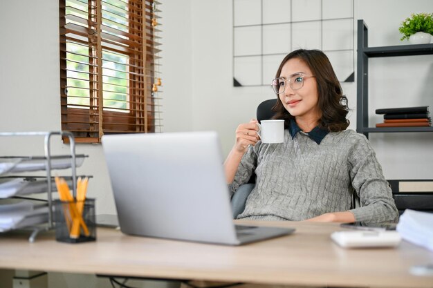 Empresária asiática bem-sucedida ou chefe feminina tomando café da manhã em sua mesa no escritório