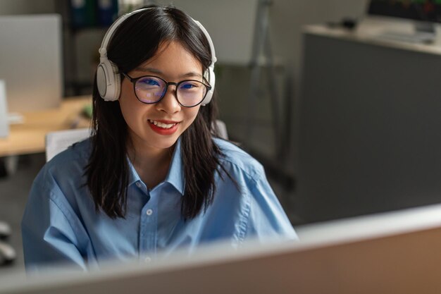 Empresária asiática bem-sucedida usando fones de ouvido no escritório