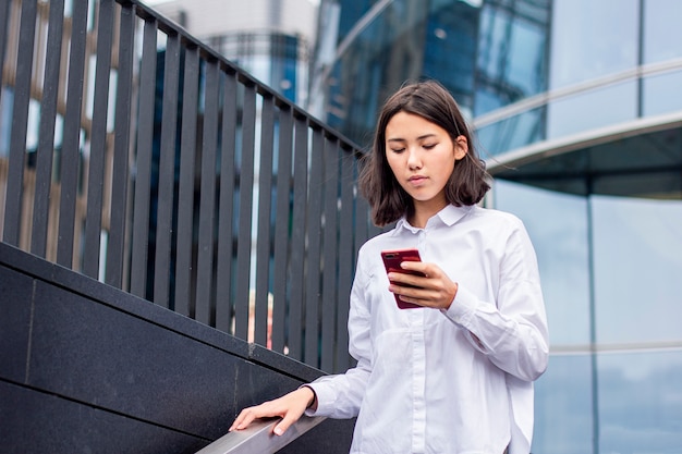 Empresaria asiática en camisa blanca usando mirando su teléfono celular