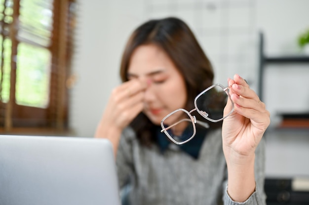 Empresária asiática cansada tirando a dor de cabeça dos óculos ou a tensão nos olhos