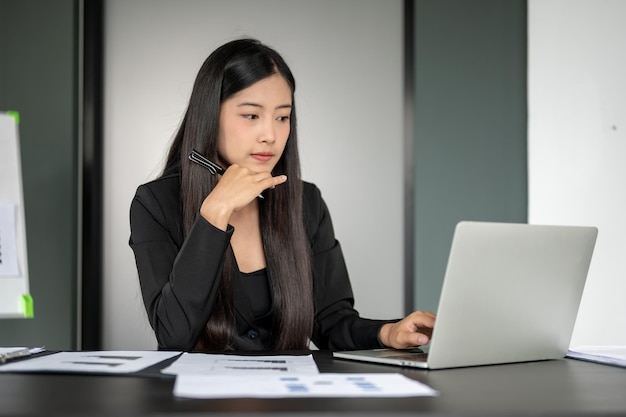 Una empresaria asiática centrada y reflexiva está trabajando en su computadora portátil en su escritorio