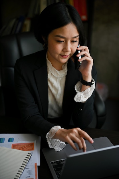 La empresaria asiática enfocada está teniendo una llamada telefónica formal de negocios en su escritorio