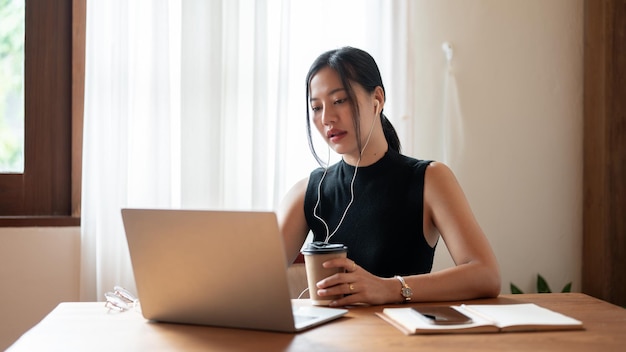 Una empresaria asiática enfocada está teniendo una reunión en línea mientras está sentada en una cafetería