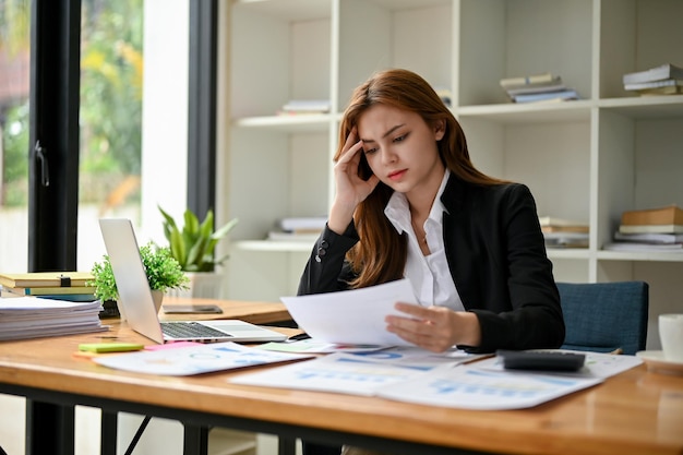 Una empresaria asiática estresada y cansada se concentra en leer y analizar informes financieros