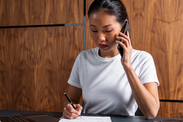 Empresária asiática falando ao telefone e escrevendo