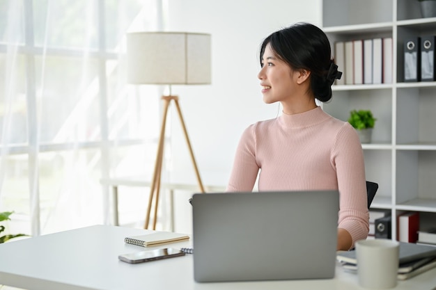 Una empresaria asiática inspirada está mirando por la ventana soñando despierta