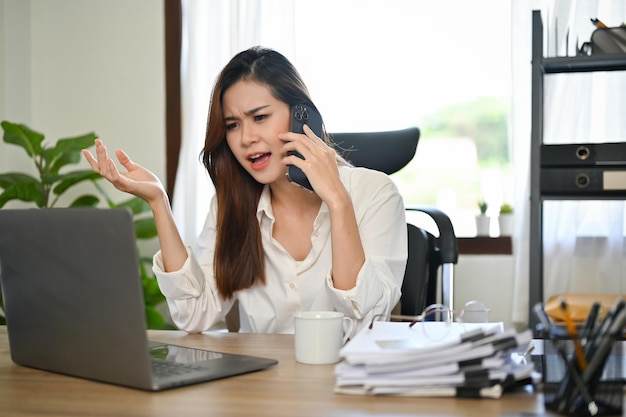 Empresária asiática irritada e insatisfeita reclamando com seu assistente no telefone