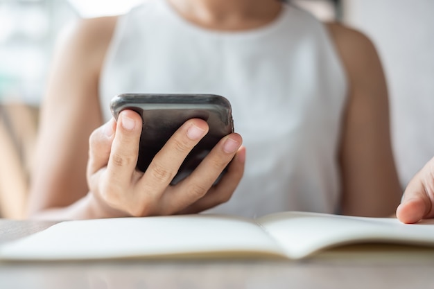 Empresaria asiática joven que usa el teléfono móvil en la oficina, la sentada de la mujer y la pantalla táctil de la mano en el teléfono móvil