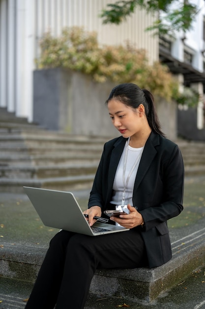 Una empresaria asiática profesional está trabajando en su computadora portátil mientras está sentada en las escaleras de la ciudad