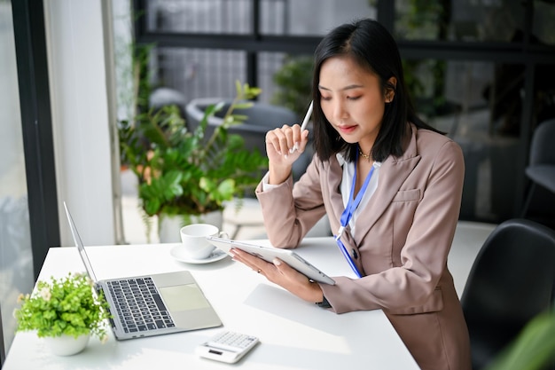 Empresaria asiática profesional que se centra en sus tareas comerciales en una tableta que trabaja en su escritorio