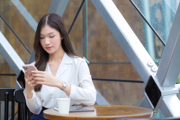 Empresária asiática profissional com cabelo comprido enquanto trabalhava fora do escritório está usando smartphone