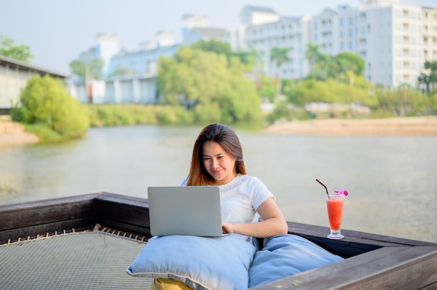 Empresaria asiática que trabaja en línea en la playa. Freelancer que usa la tecnología para trabajar en todas partes. Nuevo estilo de vida normal después de Covid-19.