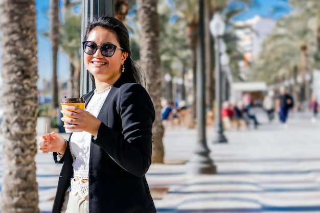 Empresária asiática sorridente em traje profissional, desfrutando de um café para viagem