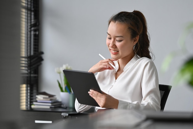 Empresária asiática sorridente recebendo boas notícias lendo informações no tablet digital