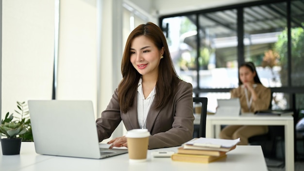 Empresária asiática sorridente trabalhando em sua tarefa em seu laptop em sua mesa