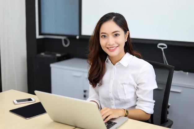 Empresária asiática sorrindo e usando seu laptop para trabalhar e fazendo pesquisas na internet em seu escritório