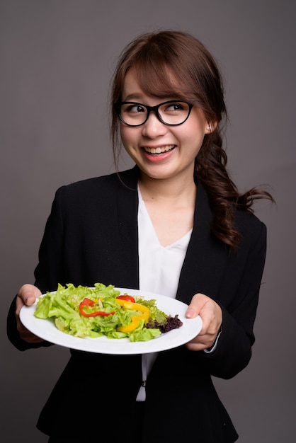 Empresaria asiática sosteniendo ensalada mientras sonríe y piensa
