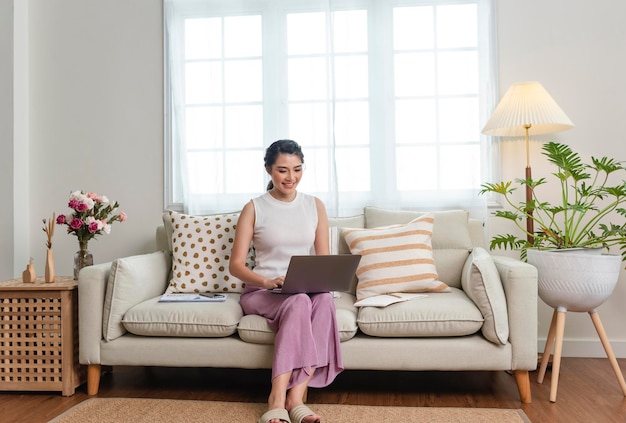 Empresária asiática usando computador portátil enquanto relaxa em um sofá em casa trabalha em casa conceito