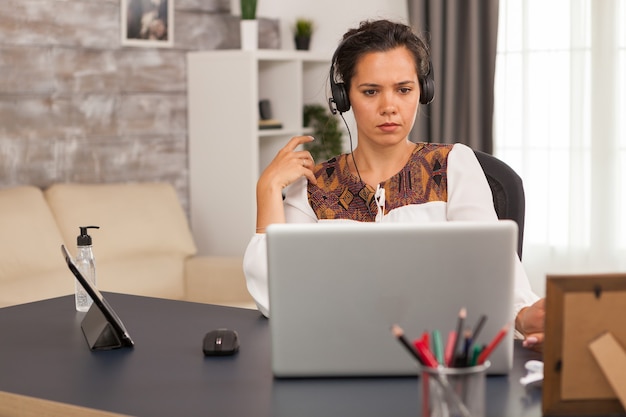 Empresaria con auriculares durante una videollamada mientras trabaja desde la oficina en casa.