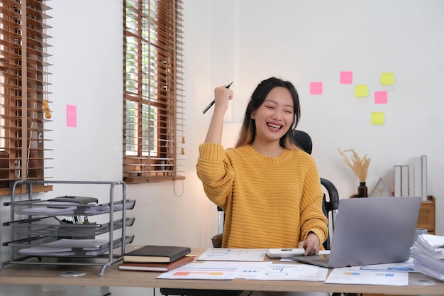 Empresária bastante asiática sentada em um laptop E o trabalho saiu com sucesso e o objetivo foi alcançado feliz e satisfeito com ela