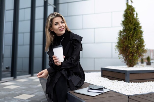 Empresária bem-sucedida de meia-idade bebendo café ao lado de um prédio de escritórios durante o almoço