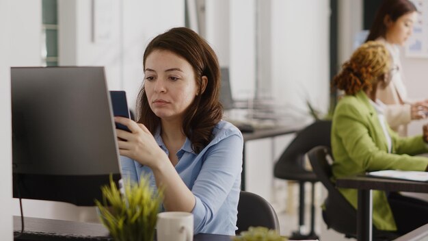 Empresária bem-sucedida fazendo uma pausa nas mídias sociais na mesa, verificando o site on-line no aplicativo para smartphone. Jovem gerente usando telefone celular e planejando o projeto de investimento. Tiro portátil.