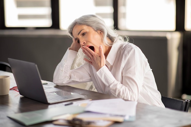 Empresária bocejando olhando para laptop cansado do trabalho de escritório interno