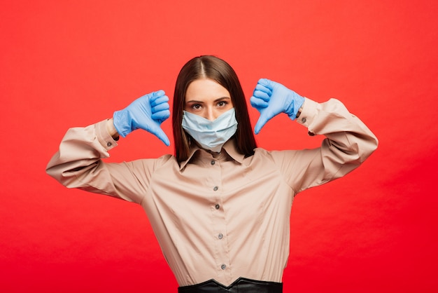 Empresária bonita emocional na máscara médica e luvas mostrando os polegares para baixo