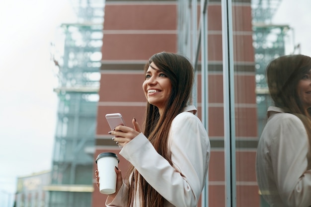 Empresaria con café y hablando por teléfono cerca de la oficina