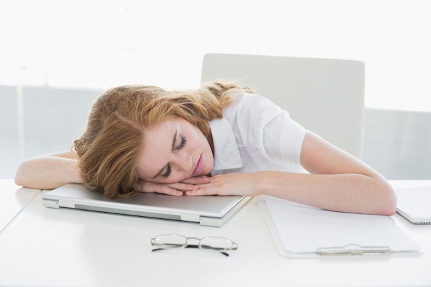 Empresaria cansada con la cabeza en la computadora portátil en la oficina