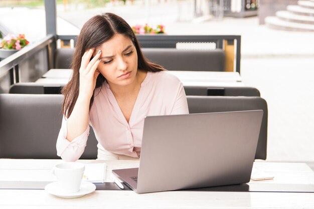 Empresaria cansada o estudiante agotado en la cafetería mirando a la pantalla de la computadora