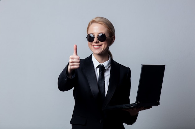 Empresaria en un clásico traje negro y gafas de sol con ordenador portátil