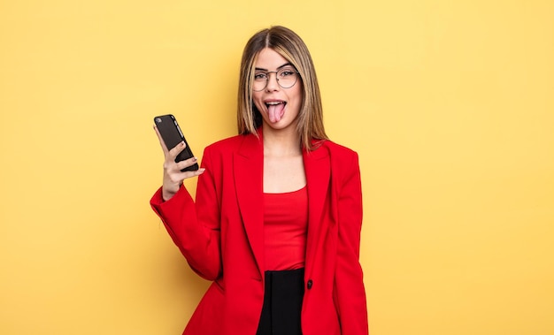 Empresária com atitude alegre e rebelde brincando e enfiando a língua para fora do conceito de smartphone