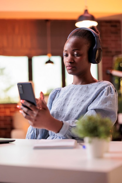 Empresária conversando com colegas de trabalho na reunião on-line do smartphone no escritório em casa moderno com luz do sol quente. Trabalhadora remota sorridente segurando o celular e conversando na teleconferência