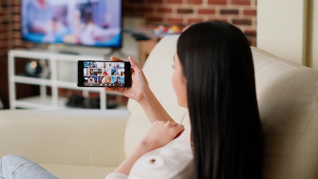 Empresária conversando com colegas de trabalho por videoconferência digital em smartphone enquanto trabalhava remotamente. Mulher trabalhando em casa enquanto discute com colegas na videoconferência digital.