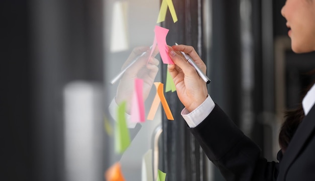 Empresaria creativa escribiendo en notas adhesivas en una pared de vidrio