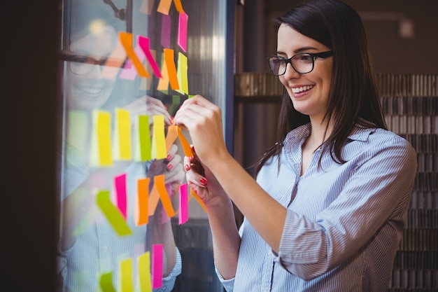 Empresaria creativa pegando notas adhesivas al vidrio en la oficina