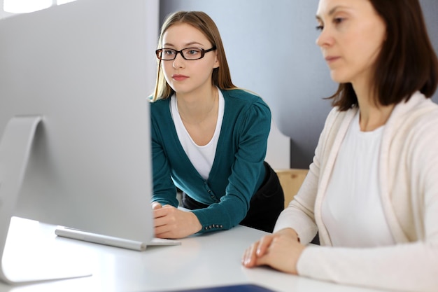 Empresária dando apresentação para sua colega enquanto eles estão sentados na mesa com o computador Grupo de empresários trabalhando no escritório Conceito de trabalho em equipe