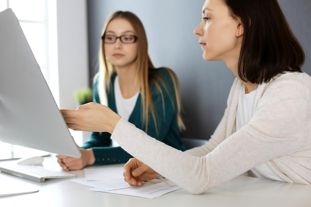 Empresária dando apresentação para sua colega enquanto eles estão sentados na mesa com o computador Grupo de empresários trabalhando no escritório Conceito de trabalho em equipe