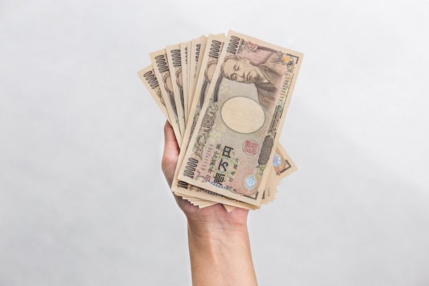 Empresaria dando dinero y sosteniendo el dinero de 10.000 yenes japoneses en la mano aislado en blanco