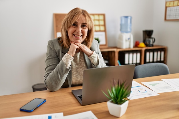 Empresária de meia-idade sorrindo feliz trabalhando no escritório