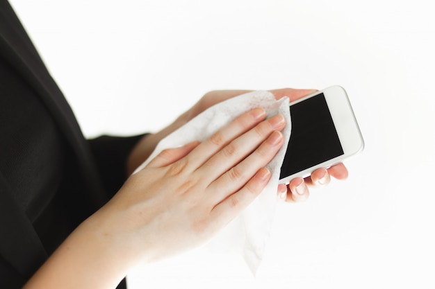 Empresária de mulher bonita em uma máscara protetora de vírus médico limpa seu telefone com toalhetes antibacterianos. precauções para uma pandemia. fechar plano de mão