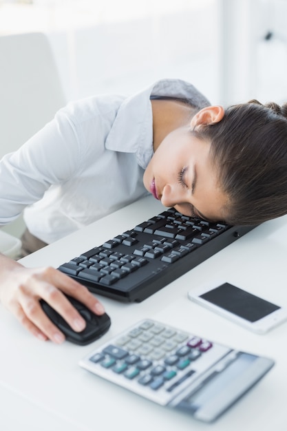 Empresaria descansando la cabeza en el teclado en la oficina