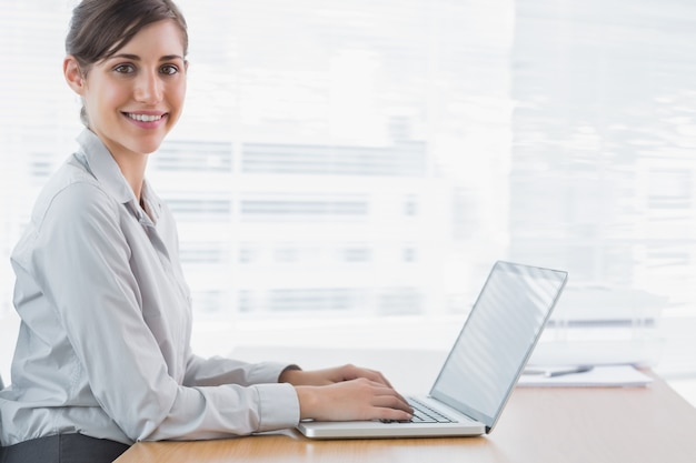 Empresária digitando em seu laptop na mesa e sorrindo para a câmera