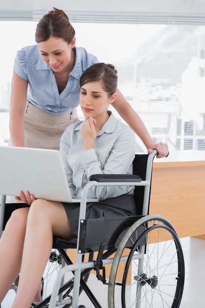 Empresaria con discapacidad mirando portátil con su colega