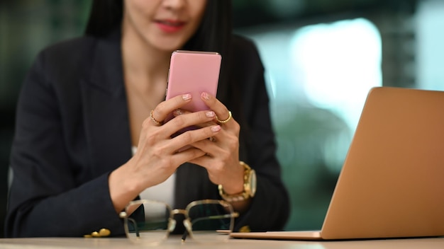 Empresária do milênio sentada na frente do laptop e verificando o aplicativo social em seu telefone inteligente