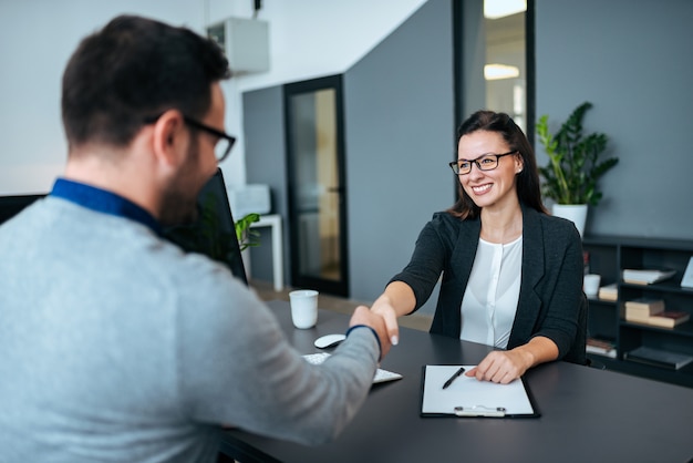 Empresária e empresário apertando as mãos no escritório moderno.