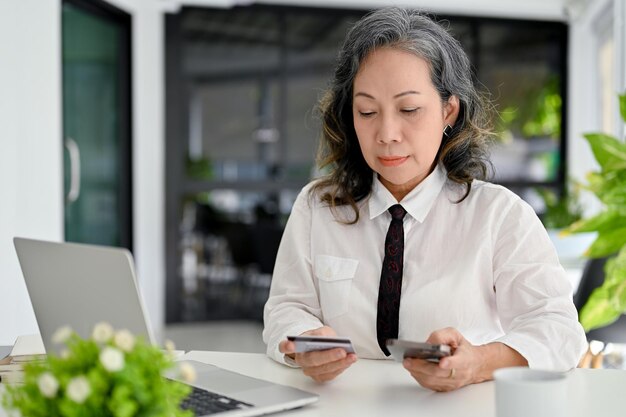 Empresaria de edad asiática que usa su teléfono inteligente para pagar facturas en línea o transferir dinero