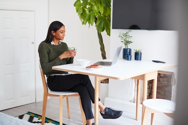 Empresária em casa tomando café da manhã olhando para laptop antes de sair para o trabalho